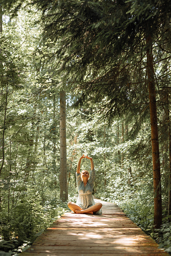 Young woman sitting in lotus position and doing breathing exercises in park. Active lifestyle concept.