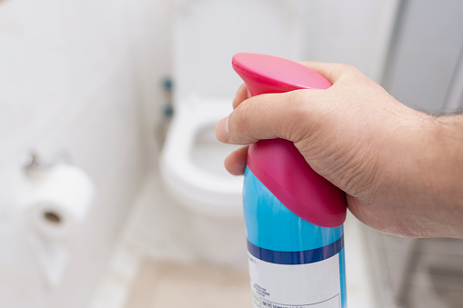 Hand sprays a toilet with air freshener