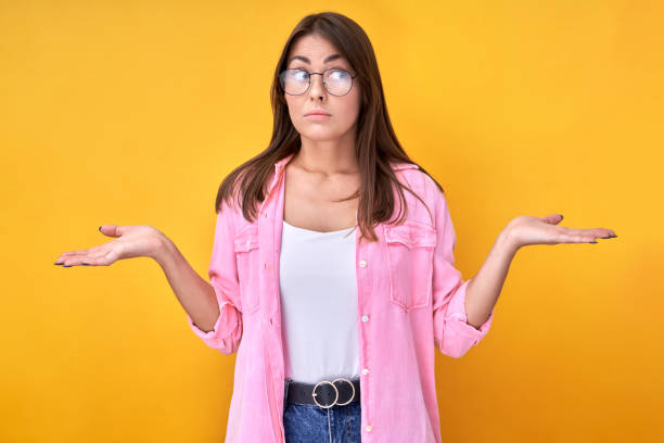istock Young woman in glasses makes a decision with doubtful face, chooses between two things, holds hands on both sides isolated in yellow studio 1327601027