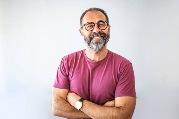 Portrait of mature businessman. Portrait of mature businessman. Male executive is wearing T-shirt. Professional is smiling against gray background. Confident businessman with arms crossed. Mature mixed race man smiling latin american and hispanic ethnicity stock pictures, royalty-free photos & images