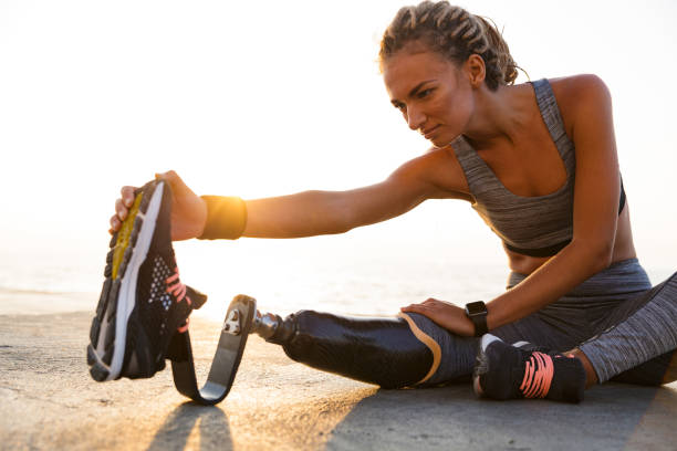 Cropped image of concentrated disabled athlete woman Cropped image of concentrated disabled athlete woman with prosthetic leg doing stretching exercises while sitting at the beach prosthetic equipment stock pictures, royalty-free photos & images