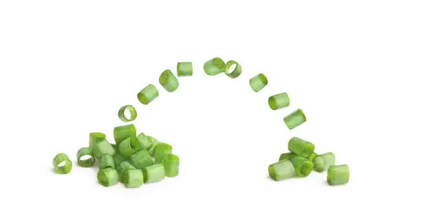 Flying slices of chopped green onion on a white background
