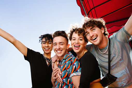 Young group of friends having fun together outdoors. Four happy queer people smiling cheerfully while standing together and embracing each other. Friends bonding and spending time together.