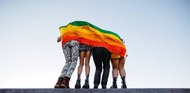 anonymous group of people standing behind a rainbow flag - gay pride flag gay pride gay man homosexual imagens e fotografias de stock