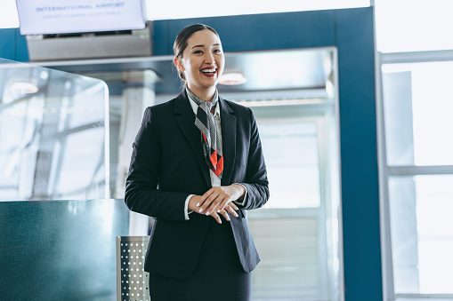 Friendly flight attendant standing at airport. Customer service representative waiting for passengers at airport.
