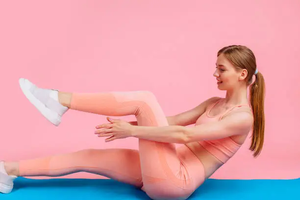 Fitness woman doing criss-cross exercise for the press lying on a sports mat, a girl in sportswear doing fitness crunches, on a pink background