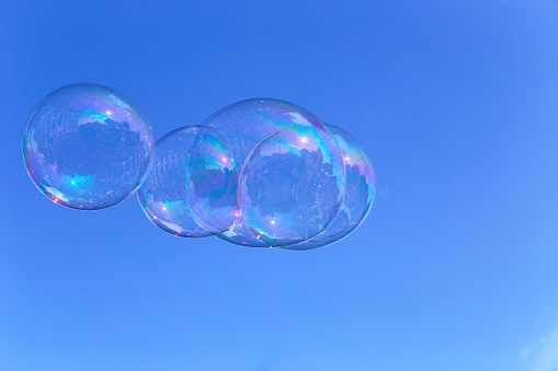 Large huge bright soap bubbles against the background of the sky and trees. Soap bubbles show. Summer children's active leisure.