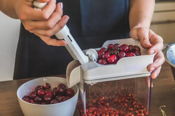Female hands pitting fresh cherries with a cherry stoner