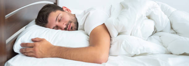 el hombre guapo durmiendo en la cama sobre el fondo blanco - wide awake fotografías e imágenes de stock