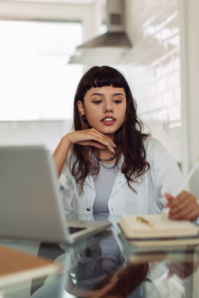 istock Focused young businesswoman making notes while working alone at her home office desk. Young businesswoman working from her laptop. Woman working from home. 1327612595