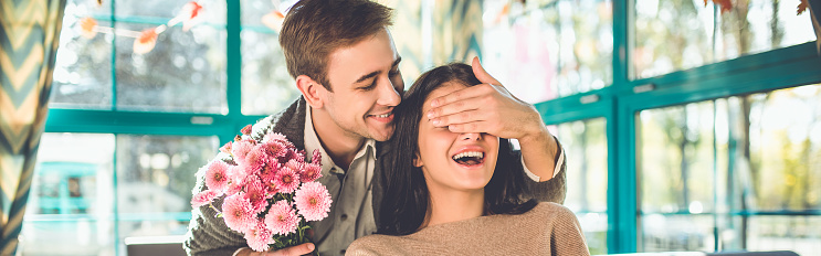 The happy man make a surprise with flowers for a woman in the restaurant