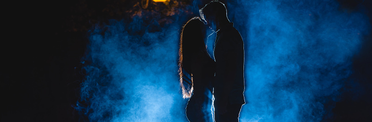 The man and woman kissing on the street on a blue smoke background. night time