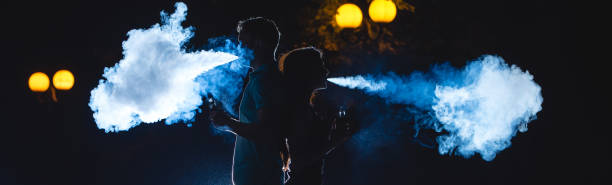 The man and woman smoke an electrical cigarette on the dark street. night time stock photo