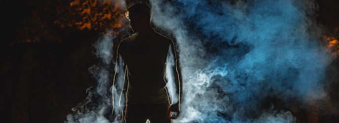 The silhouette of a man on the street on the background of a smoke. night time