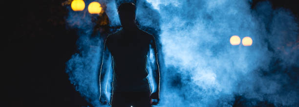 der mann steht auf dem blauen rauchhintergrund. nachtzeit - street fog profile stock-fotos und bilder