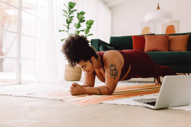 Healthy woman doing plank workout using laptop at home