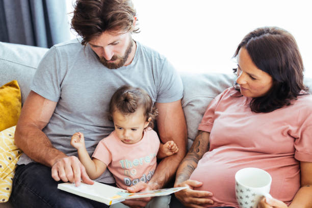 Dad and Mum reading a storybook to baby girl Father reading a story from picture book to her baby girl while pregnant mother seated besides them real wife stories stock pictures, royalty-free photos & images