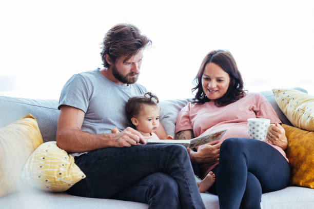 Parents reading a storybook to their toddler Father reading a story from picture book to her baby girl while pregnant mother seated besides them real wife stories stock pictures, royalty-free photos & images