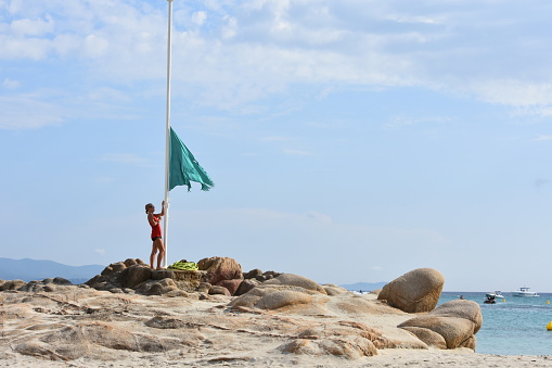 Calvi, France - August 30, 2019: The village and touristic harbor of Calvi, Corsica, in a sunny summer day. A lifeguard raises a flag at the beach