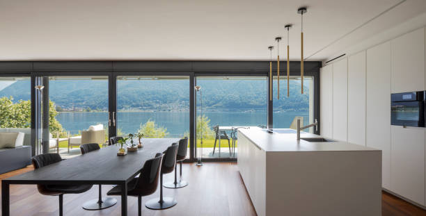 istock Interior of a modern apartment, with dining room and open kitchen. Front view. While eating you have a spectacular view of the lake. Nobody inside, the table seats six. 1327617247