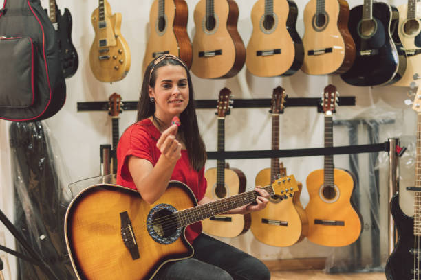 une jeune femme s’assoit dans un magasin de guitare prête à jouer - folk song photos et images de collection
