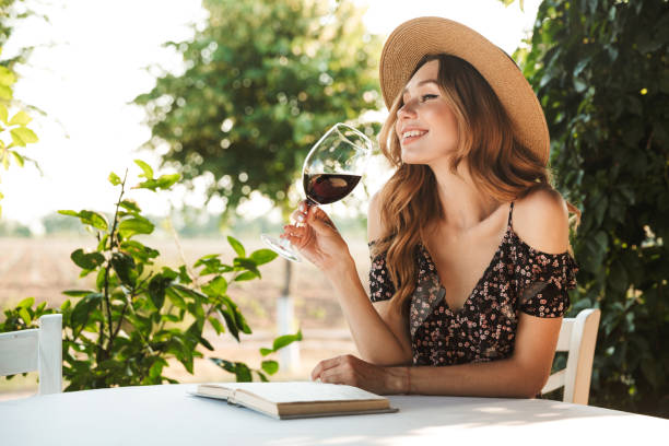 Pretty young woman drinking wine. Image of cute pretty young woman sitting in cafe outdors in park with book holding glass drinking wine. women only restaurant stock pictures, royalty-free photos & images