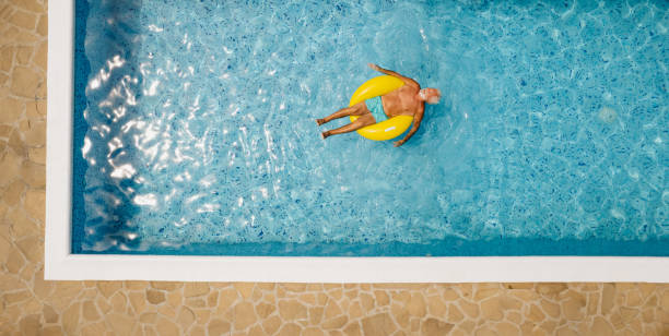 idoso em anel inflável na piscina - floating on water swimming pool men water - fotografias e filmes do acervo