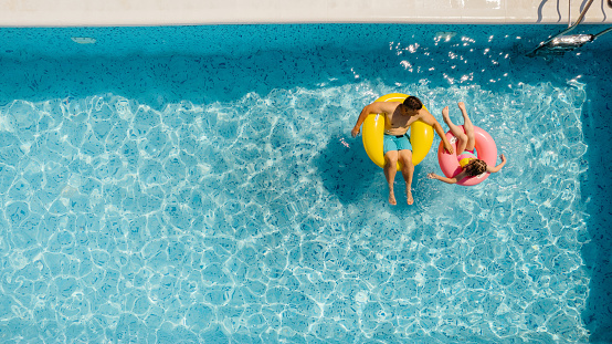 Photo of father and daughter enjoying together on the inflatable rings in the swimming pool