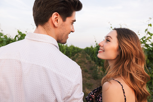 Loving young couple man and woman dating while walking outdoor together through vineyard on summer day