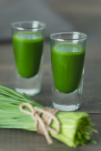 A bundle of wheatgrass with wheatgrass smoothies on wooden background.
