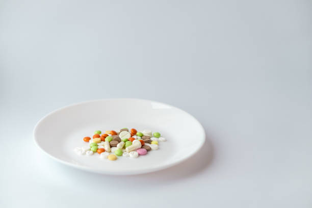istock Pills on a white plate. Multi-colored pile of pills on a white background. Medication on a white table. Pills under the guise of food on a plate. A pile of tletoks symbolizing food. 1327628010
