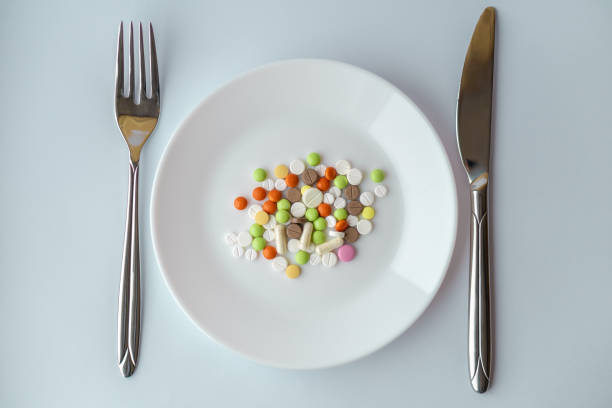 istock Pills on a white plate. Gestures with a knife and fork on a plate with pills. Medicines on a white background. A pile of multi-colored tablets disguised as food on a plate with cutlery. 1327628074