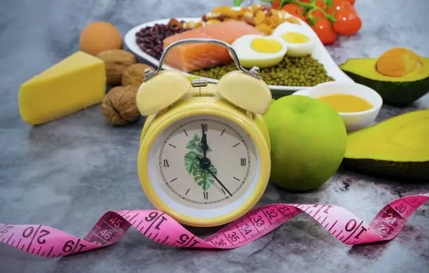 Photo of Selective focus of Alarm clock for Intermittent fasting and Healthy food which a  healthy of Keto diet food ingredients on  the  table.Ketogenic mean Low carb and High fat.