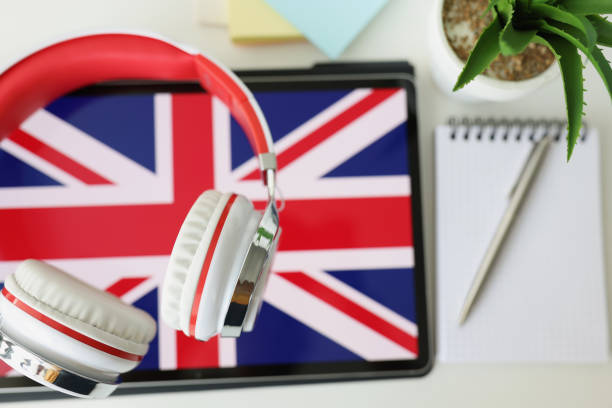 Tablet with image of British flag with headphones and notebook with pen lie on table Tablet with image of British flag with headphones and notebook with pen lie on table. Learn British English remotely via app concept english spoken stock pictures, royalty-free photos & images