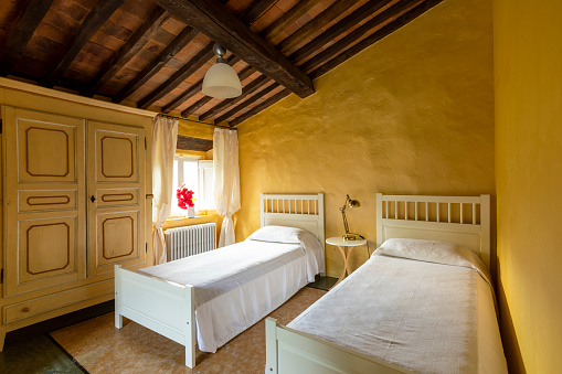 Interior of a bedroom with two single beds. Spartan ambiance and nothing luxurious. The walls are yellow.
