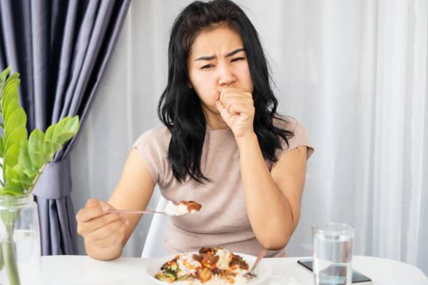 donna asiatica che soffoca mentre mangia un pasto ha del cibo bloccato in gola e cerca di vomitare o tossire - soffocare foto e immagini stock