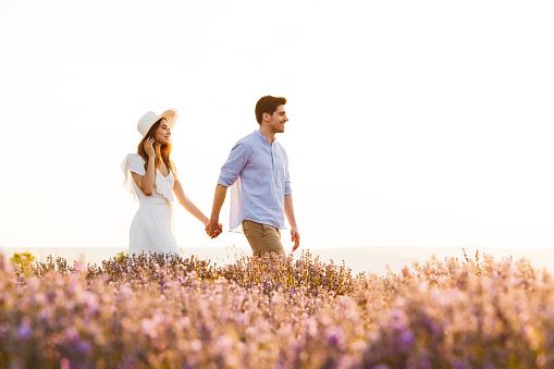 Image of happy young cute loving couple walking in the lavender field outdoors holding hands of each other.