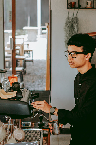 Young barista making Coffee For Customers At Cafe