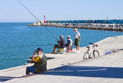 Pesaro, Italy - 9 july 2020: a little boy is fishing with his father and grandfather on the dock of the port of Pesaro
