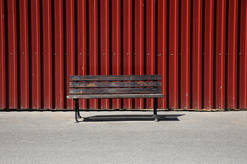 Empty sitting bench and red metal wall
