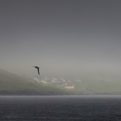 Kalsoy island seen from the ocean almost completely covered in haze but the sun just lits up the small village of Mikladalur on Faroe Islands.