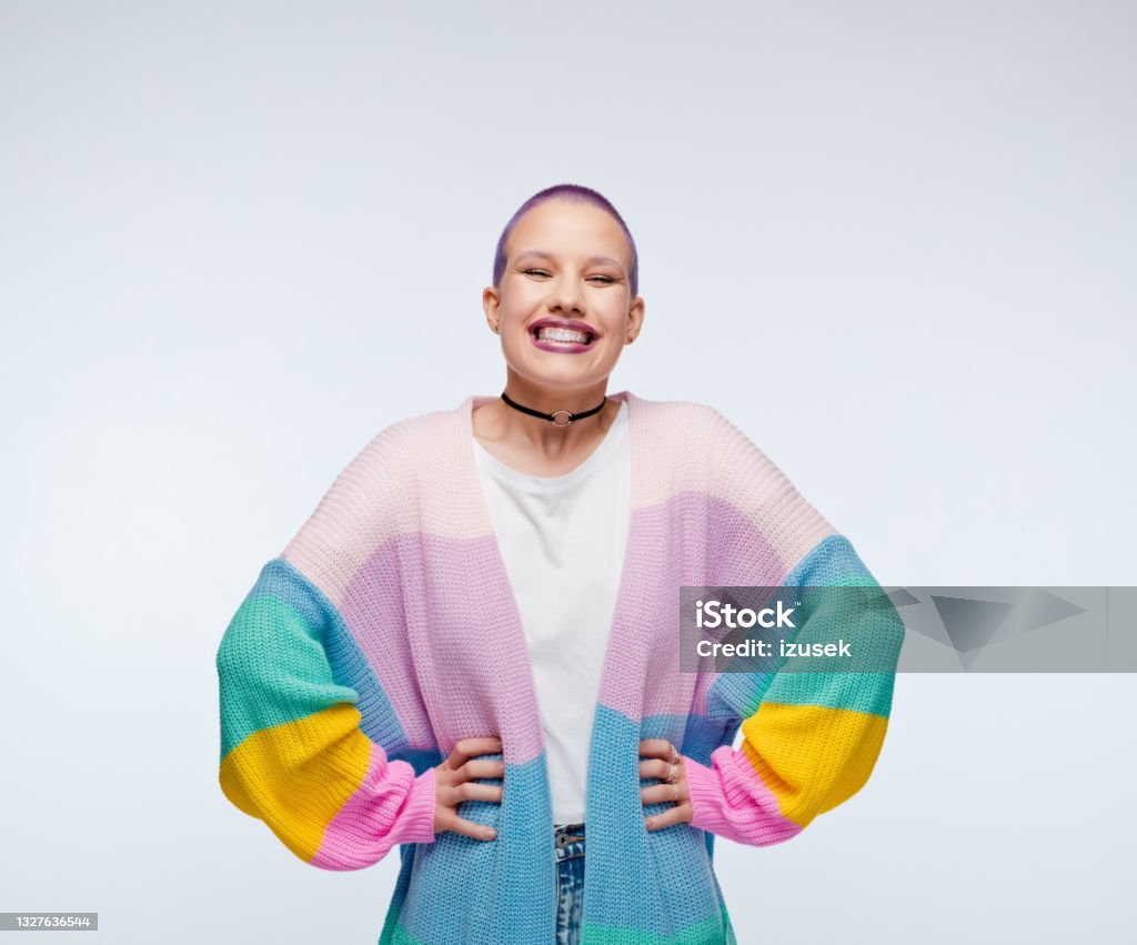 Excited woman wearing rainbow cardigan Cheerful young woman wearing rainbow cardigan standing with hands on hips and laughing at camera. Studio portrait on white background. LGBTQIA People Stock Photo