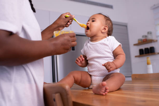 istock Adorable baby child eating pureed mango with a teaspoon. 1327637944