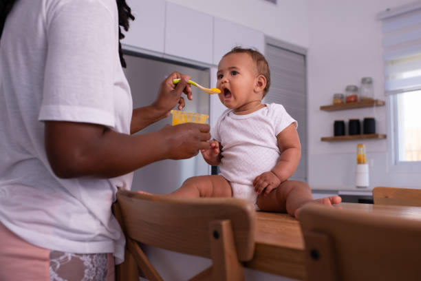 istock Adorable baby child eating pureed mango with a teaspoon. 1327638177