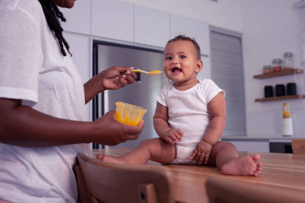 istock Adorable baby child eating pureed mango with a teaspoon. 1327638189