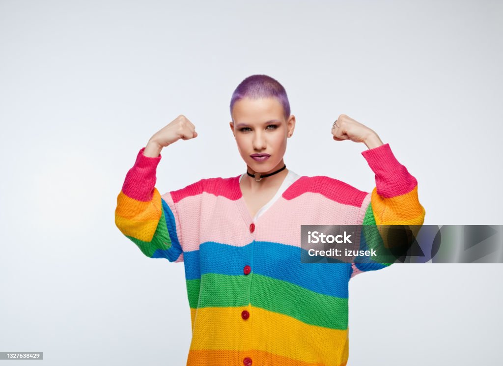 Girl power Confident young woman wearing rainbow cardigan, raising arms and flexing fists. Studio portrait on white background. Cool Attitude Stock Photo