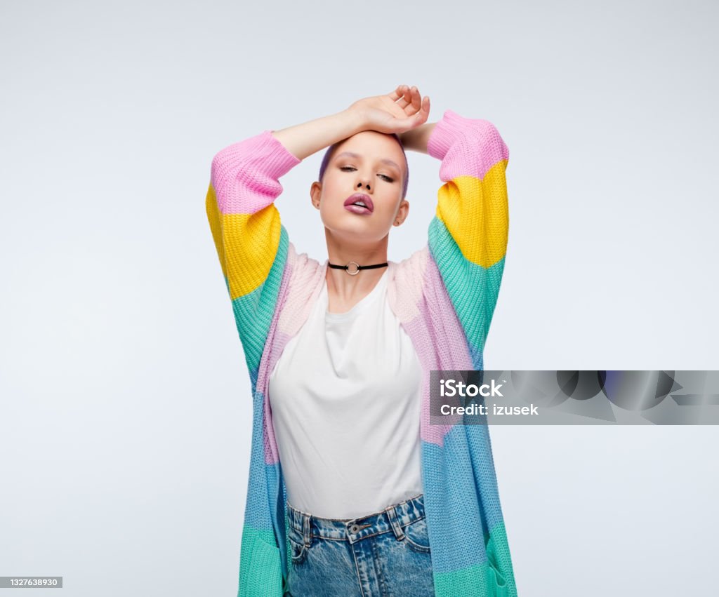 Short hair wearing rainbow cardigan Confident young woman wearing rainbow cardigan, white shirt and jeans standing with raised amrs. Studio portrait on white background. Transgender Person Stock Photo