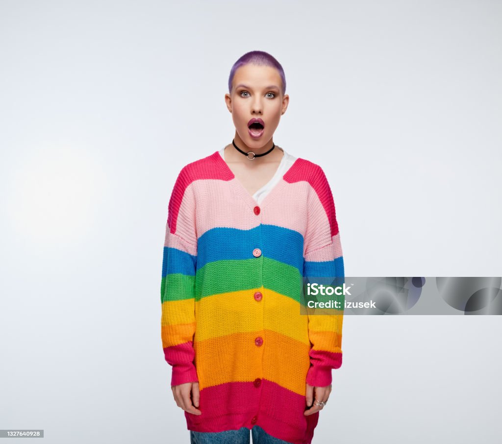 Woman with short purple hair wearing rainbow cardigan Surprised young woman wearing rainbow cardigan, staring at camera with mouth open. Studio portrait on white background. 20-29 Years Stock Photo