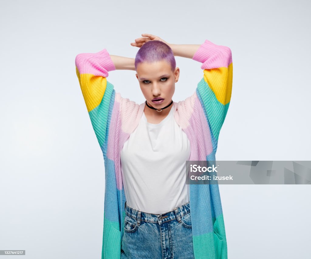 Woman with short purple hair wearing rainbow cardigan Confident young woman wearing rainbow cardigan standing with raised arms and looking at camera. Studio portrait on white background. Effortless Stock Photo