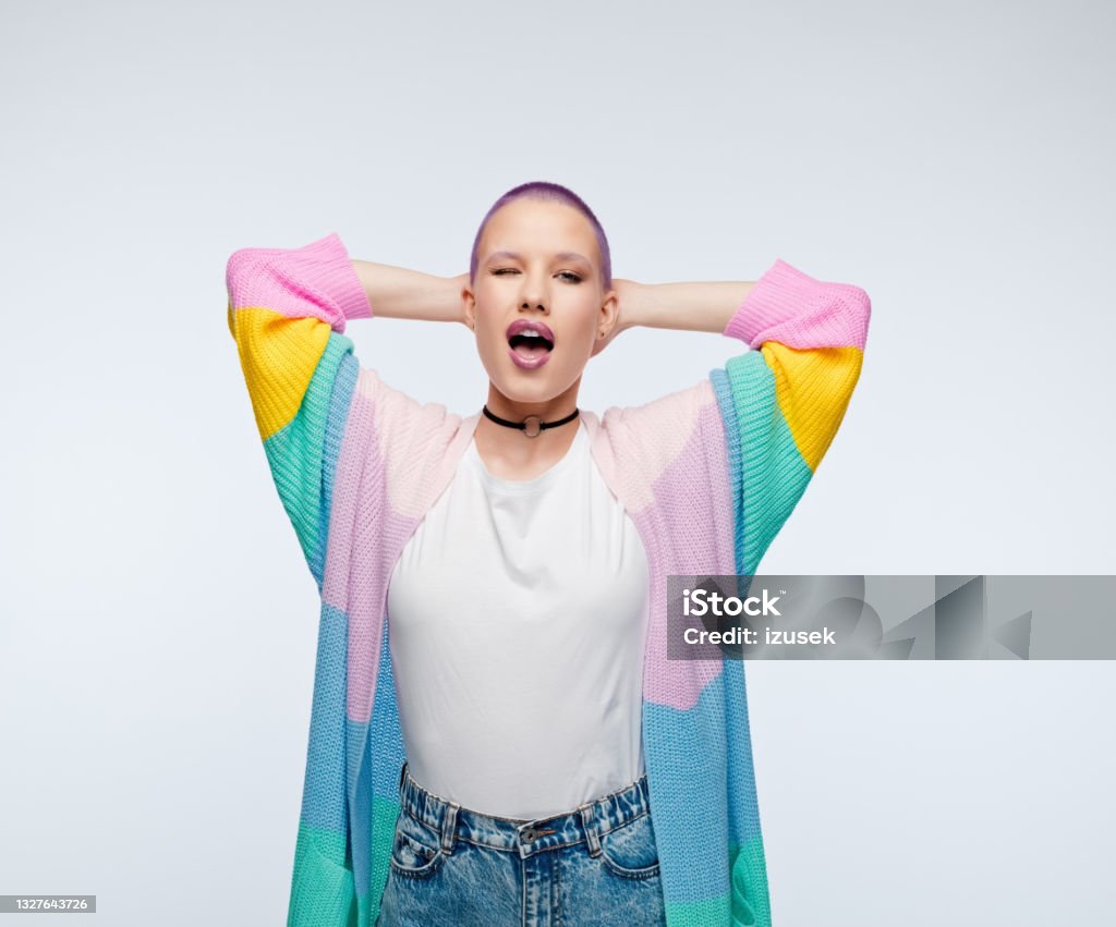 Woman with short purple hair wearing rainbow cardigan Cheerful young woman wearing rainbow cardigan standing with raised arms, blinking eye. Studio portrait on white background. One Woman Only Stock Photo